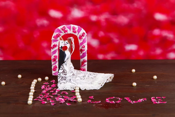 Decoratieve getrouwd liefdevol paar op houten tafel op rode achtergrond — Stockfoto