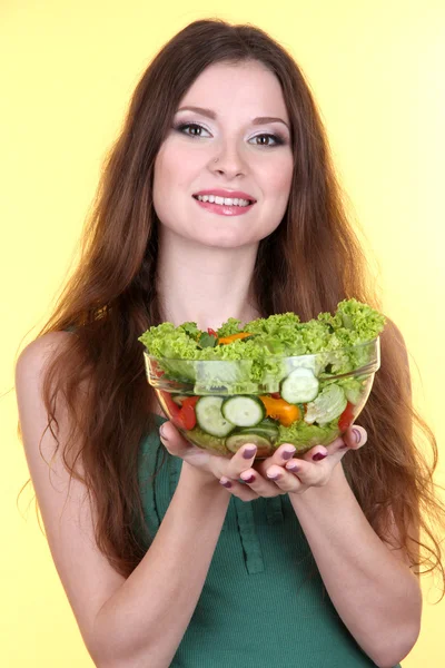 Hermosa mujer con ensalada de verduras sobre fondo amarillo — Foto de Stock