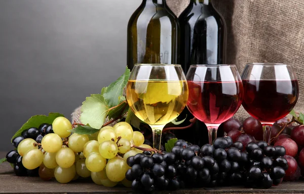 Bottiglie e calici di vino e uva su fondo grigio — Foto Stock