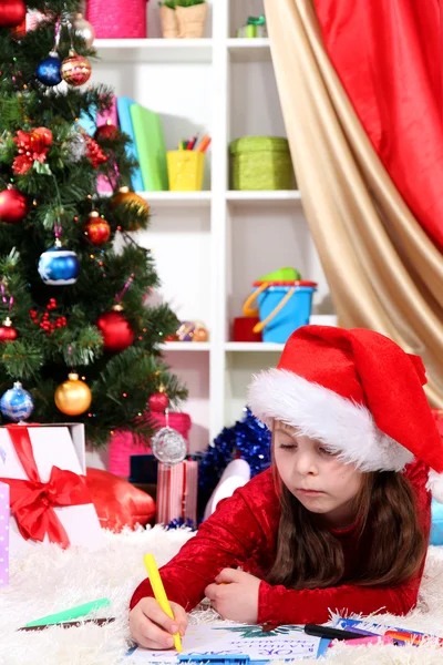 Beautiful little girl writes letter to Santa Claus in festively decorated room Stock Picture