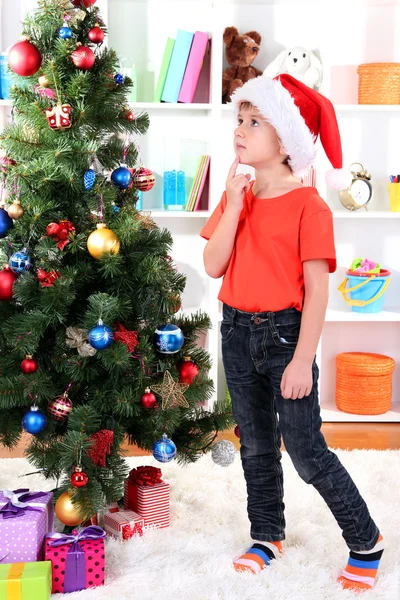 Little boy in Santa hat dreams near Christmas tree Stock Photo