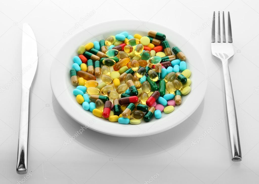Colorful Capsules And Pills On Plate With Fork And Knife Isolated
