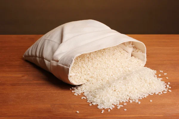 Cloth bag of rice on wooden table on brown background — Stock Photo, Image