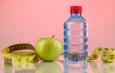 şişe su, elma ve pembe bir arka plan üzerinde ölçüm bandı