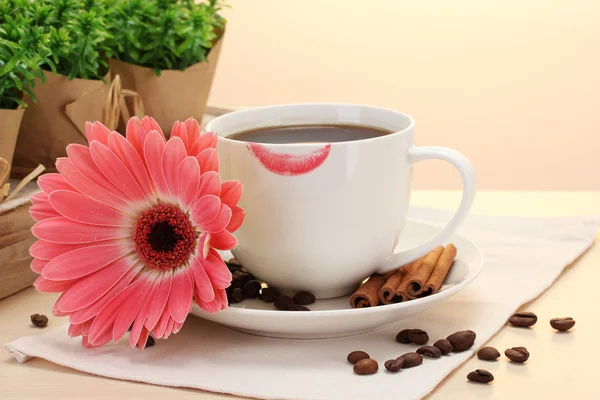 Taza de café con marca de lápiz labial y granos de gerberas, palitos de canela en la mesa de madera —  Fotos de Stock