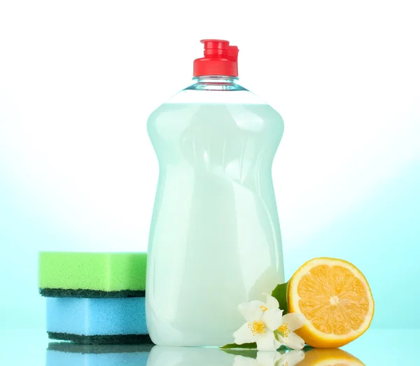 Líquido de lavagem de pratos com esponjas e limão com flores em fundo azul — Fotografia de Stock