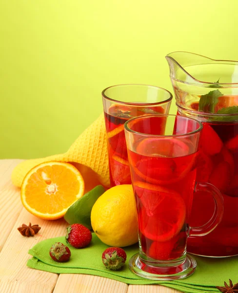 Sangria in jar and glasses with fruits, on wooden table, on green background — Stock Photo, Image