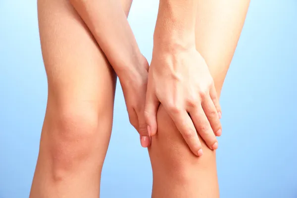 Frau mit schmerzenden Knien, auf blauem Hintergrund — Stockfoto