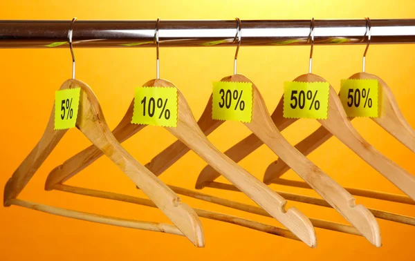 Wooden clothes hangers as sale symbol on orange background — Stock Photo, Image