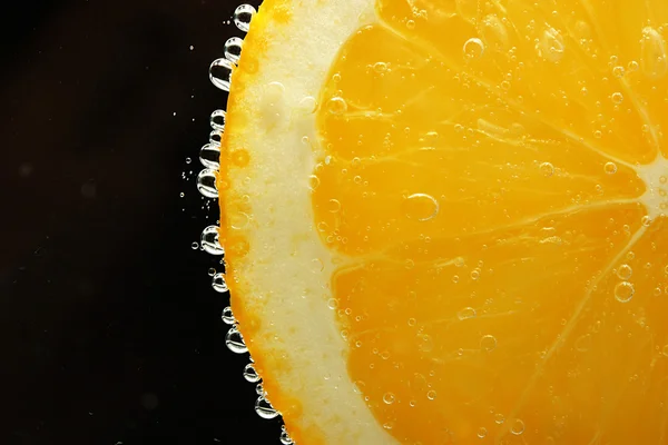 Rebanada de naranja en el agua con burbujas, sobre fondo negro — Foto de Stock