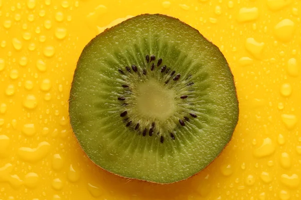 Slice of kiwi with drop on yellow background — Stock Photo, Image