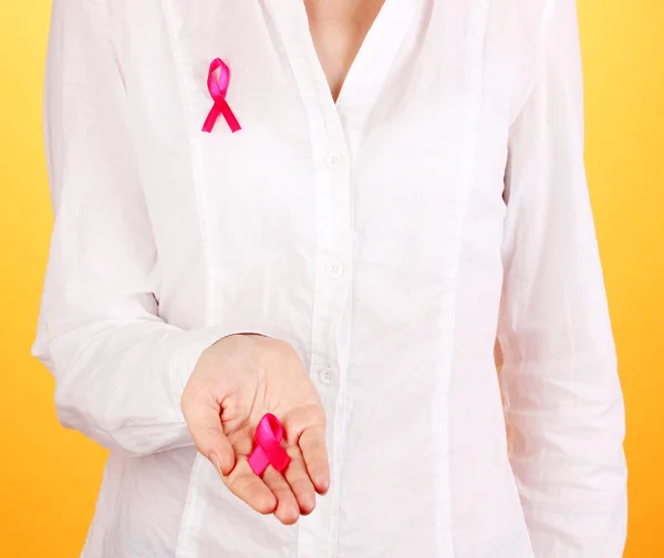 Frau mit rosa Schleife in den Händen auf orangefarbenem Hintergrund — Stockfoto