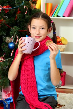 sıcak bir içecek yılbaşı ağacının yanında oturan bir pembe eşarp ve küçük kız