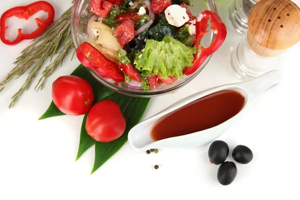 Tuore kreikkalainen salaatti lasikulhossa, jota ympäröivät ruoanlaittoon tarkoitetut ainekset, jotka on eristetty valkoisella — kuvapankkivalokuva