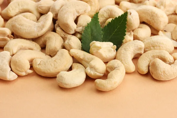 Вкусные орехи кешью с зелеными листьями, на бежевом фоне — стоковое фото