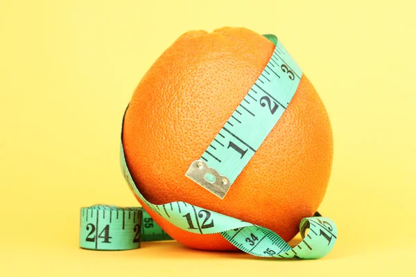 Orange with measuring tape on yellow background — Stock Photo, Image