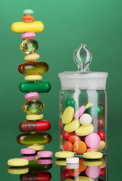 Capsules and pills hill and in receptacle on green background — Stock Photo, Image