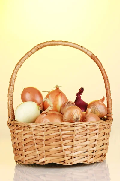 Reife Zwiebeln im Korb auf gelbem Hintergrund — Stockfoto