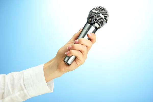 Mano femminile con microfono, su sfondo blu — Foto Stock