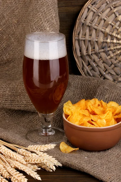 Vaso de cerveza con plato de patatas fritas sobre mesa de madera sobre fondo de saco — Foto de Stock