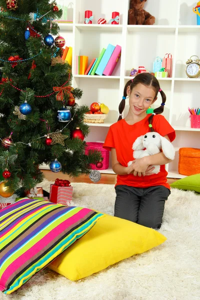 Klein meisje houdt van speelgoed in de buurt van de kerstboom — Stockfoto