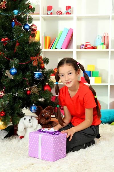 Liten flicka håller presentförpackning nära julgran — Stockfoto