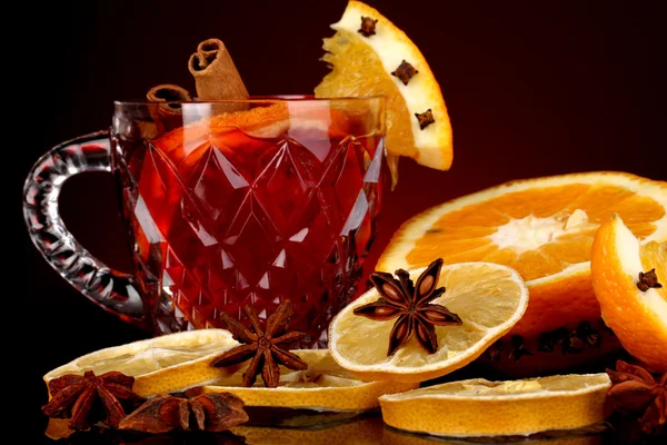 Αρωματικά mulled κρασί σε ποτήρι με μπαχαρικά και τα πορτοκάλια γύρω σε κόκκινο φόντο — Φωτογραφία Αρχείου