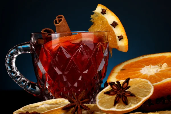 Duftender Glühwein im Glas mit Gewürzen und Orangen auf blauem Hintergrund — Stockfoto