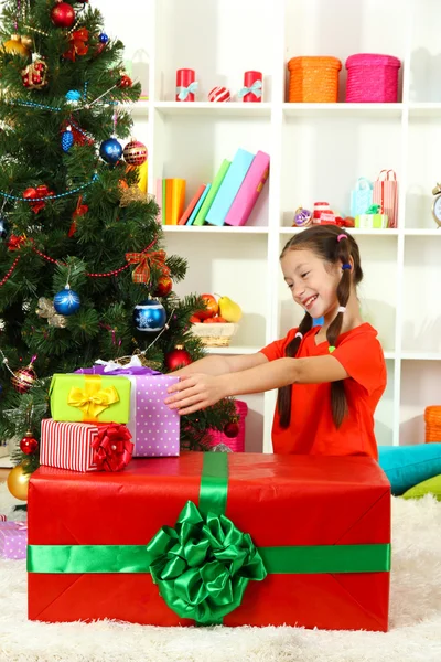 Little girl with large gift box near christmas tree Stock Picture