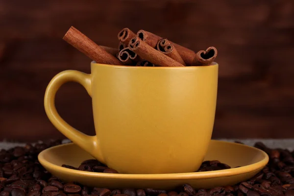 Склад жовтої чашки з кавовими зернами та корицею на дерев'яному фоні — стокове фото