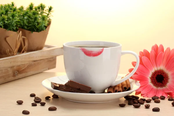 Cup of coffee with lipstick mark and gerbera beans, cinnamon sticks on wooden table — Stock Photo, Image