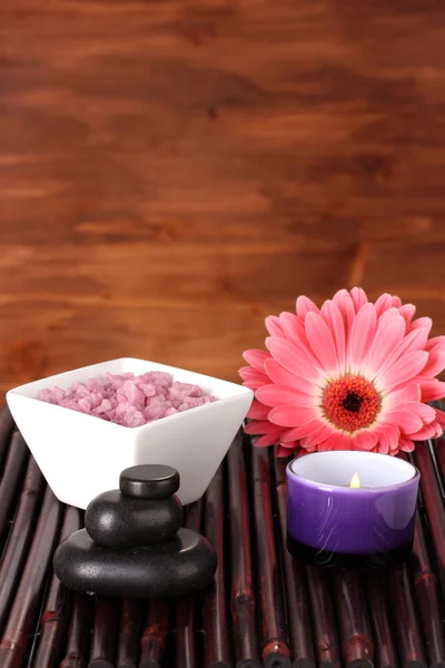 Composition of spa stones, bath salt, candle and gerbera on bamboo mat on wooden background — Stock Photo, Image