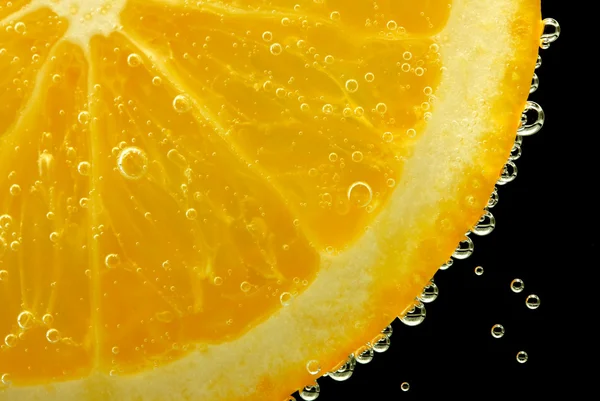 Skive oransje i vannet med bobler, på svart bakgrunn – stockfoto