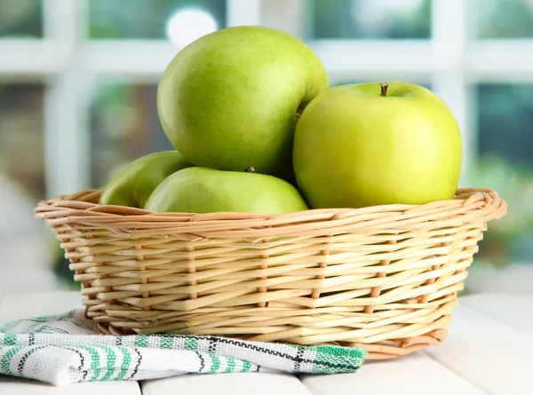 Dojrzałe jabłka zielone z liści w koszyku, na drewnianym stole, na tle okna — Zdjęcie stockowe