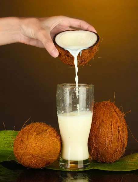 Woman's hand pouring coconut milk into a glass on brown background — Stock Photo, Image