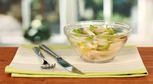 Салат из колец кальмара, лимона и салата в стеклянной миске на деревянном столе крупным планом — стоковое фото