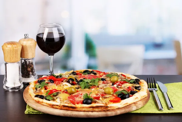Delicious pizza with glass of red wine and spices on wooden table on room background — Stock Photo, Image