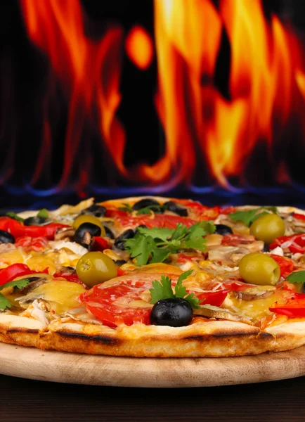 Heerlijke pizza close-up op houten tafel op brand achtergrond — Stockfoto