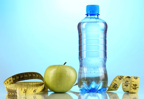 Fles water, apple en meetband op blauwe achtergrond — Stockfoto