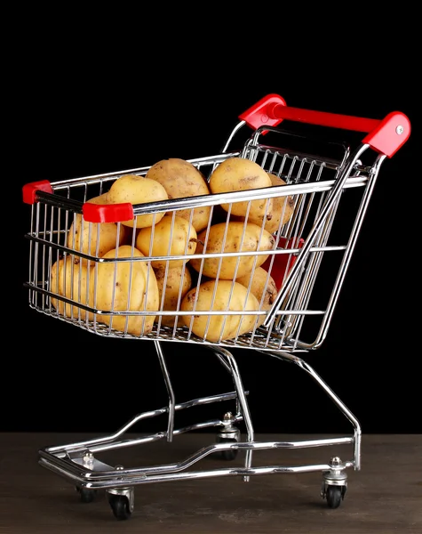 Ripe potatoes in trolley on wooden table on black background — Stock Photo, Image