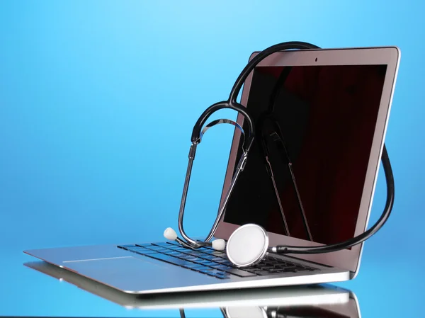 Zilveren laptop met een stethoscoop op blauwe achtergrond met reflectie — Stockfoto
