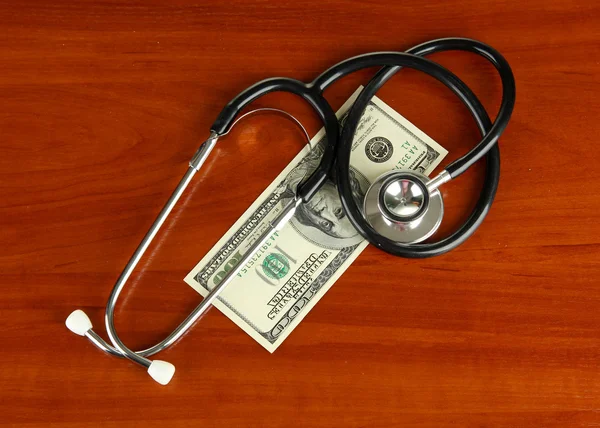 Concept de coût des soins de santé : stéthoscope et dollars sur fond de bois — Photo