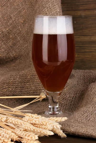 Vaso de cerveza sobre mesa de madera sobre fondo de saco —  Fotos de Stock