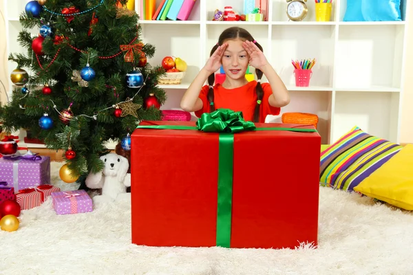 Kleines Mädchen mit großer Geschenkschachtel in der Nähe des Weihnachtsbaums — Stockfoto