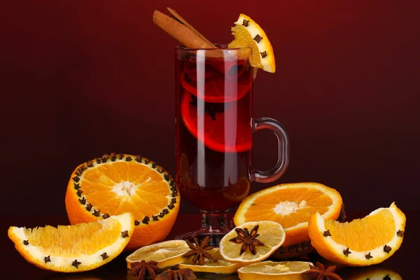 Pachnące grzane wino w szkle z przyprawami i pomarańcze wokół na czerwonym tle — Zdjęcie stockowe