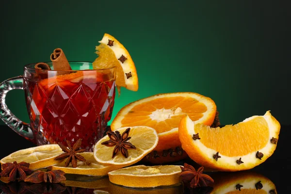 Duftender Glühwein im Glas mit Gewürzen und Orangen auf grünem Hintergrund — Stockfoto