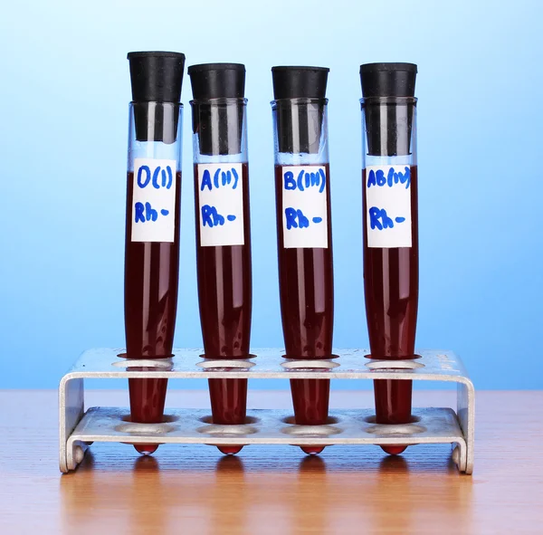 Test-tubes with blood on wooden table on blue background — Stock Photo, Image