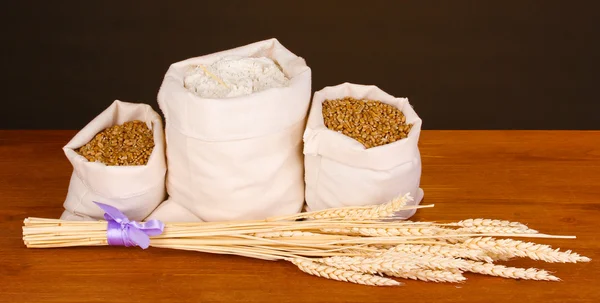 Flour and wheat grain on wooden table on dark background — Stock Photo, Image