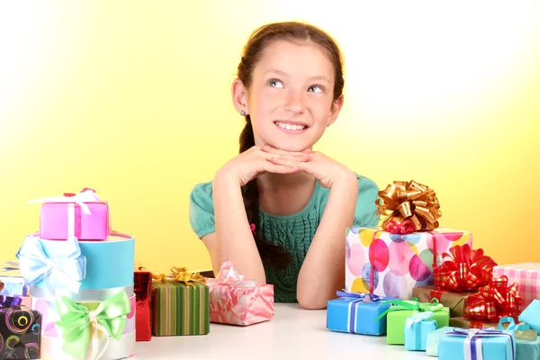 Little girl with gifts on yellow background — Stock Photo, Image