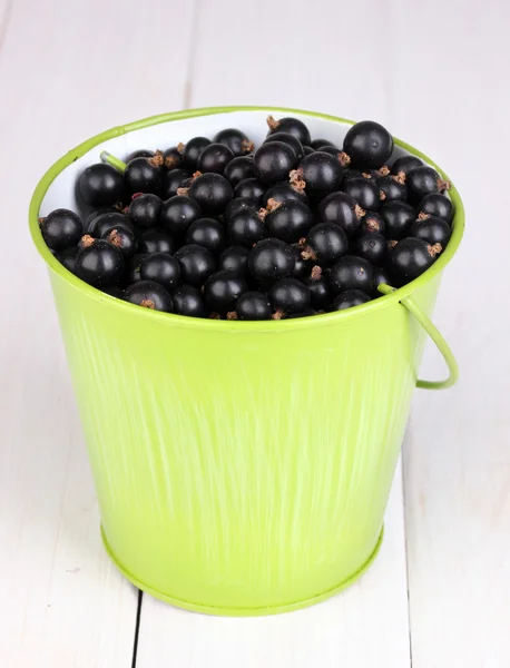 Black currant in metal bucket on wooden background